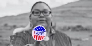 A photo of a native American holding an I voted sticker